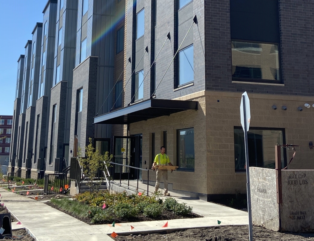 A person in safety yellow walks out of a multifamily building.